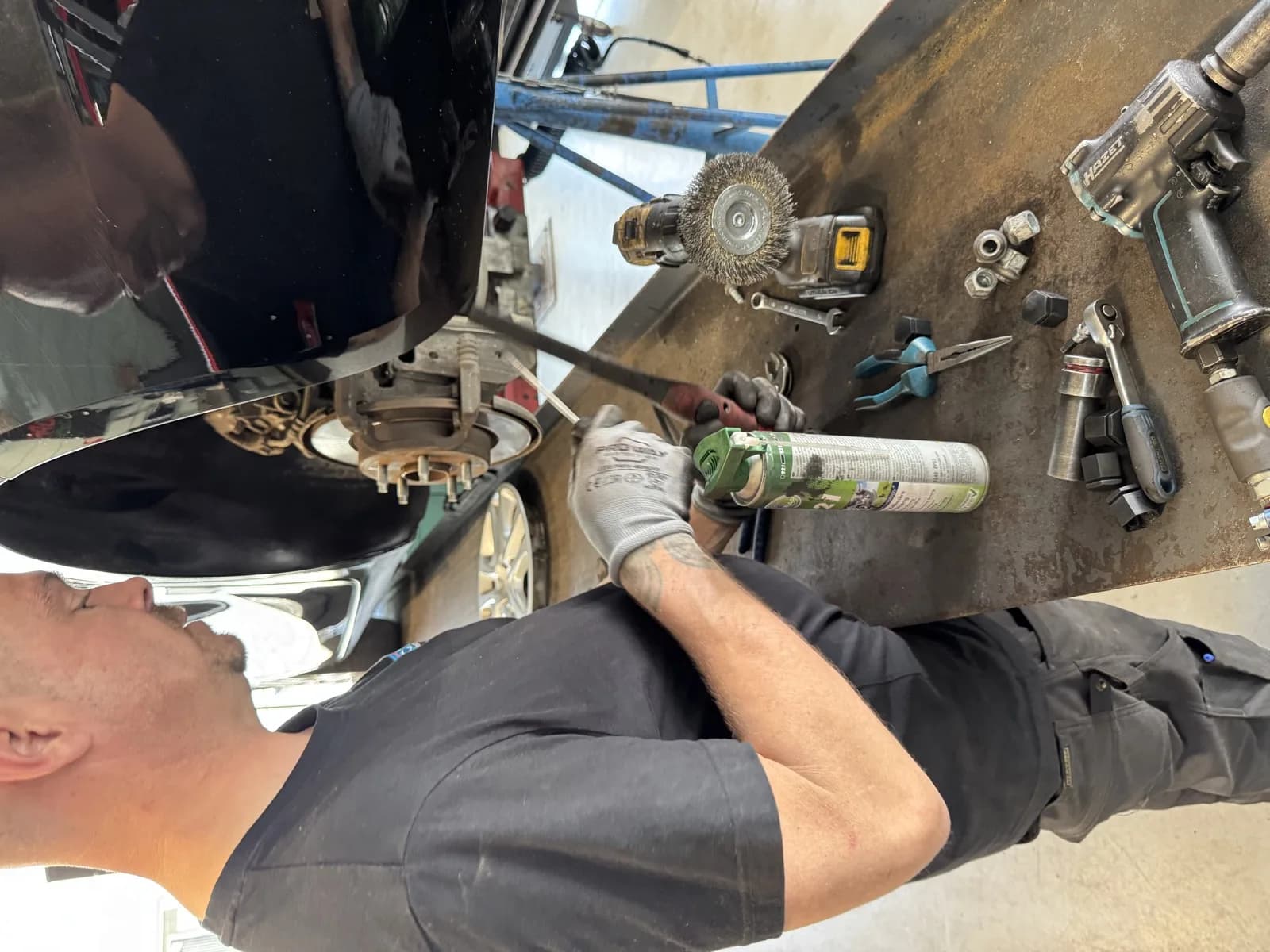 Monteur met spuitbus voor airco reiniging onder auto — airco reinigen en ozon behandeling MTechniek Alkmaar
