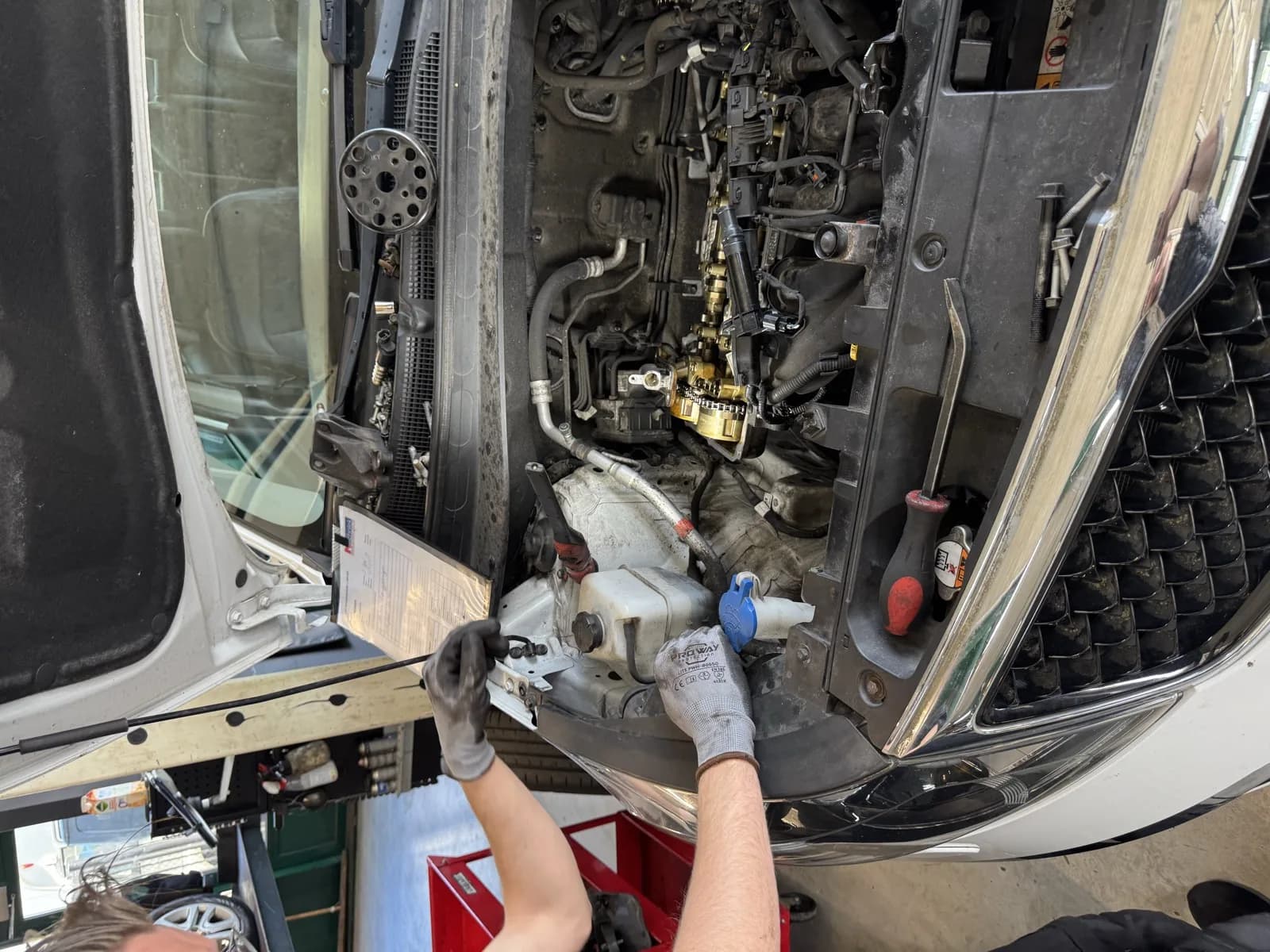 Monteur met handschoenen werkt aan de motorruimte van een auto in de werkplaats van MTechniek Alkmaar, met zicht op verstuivers en brandstofrail