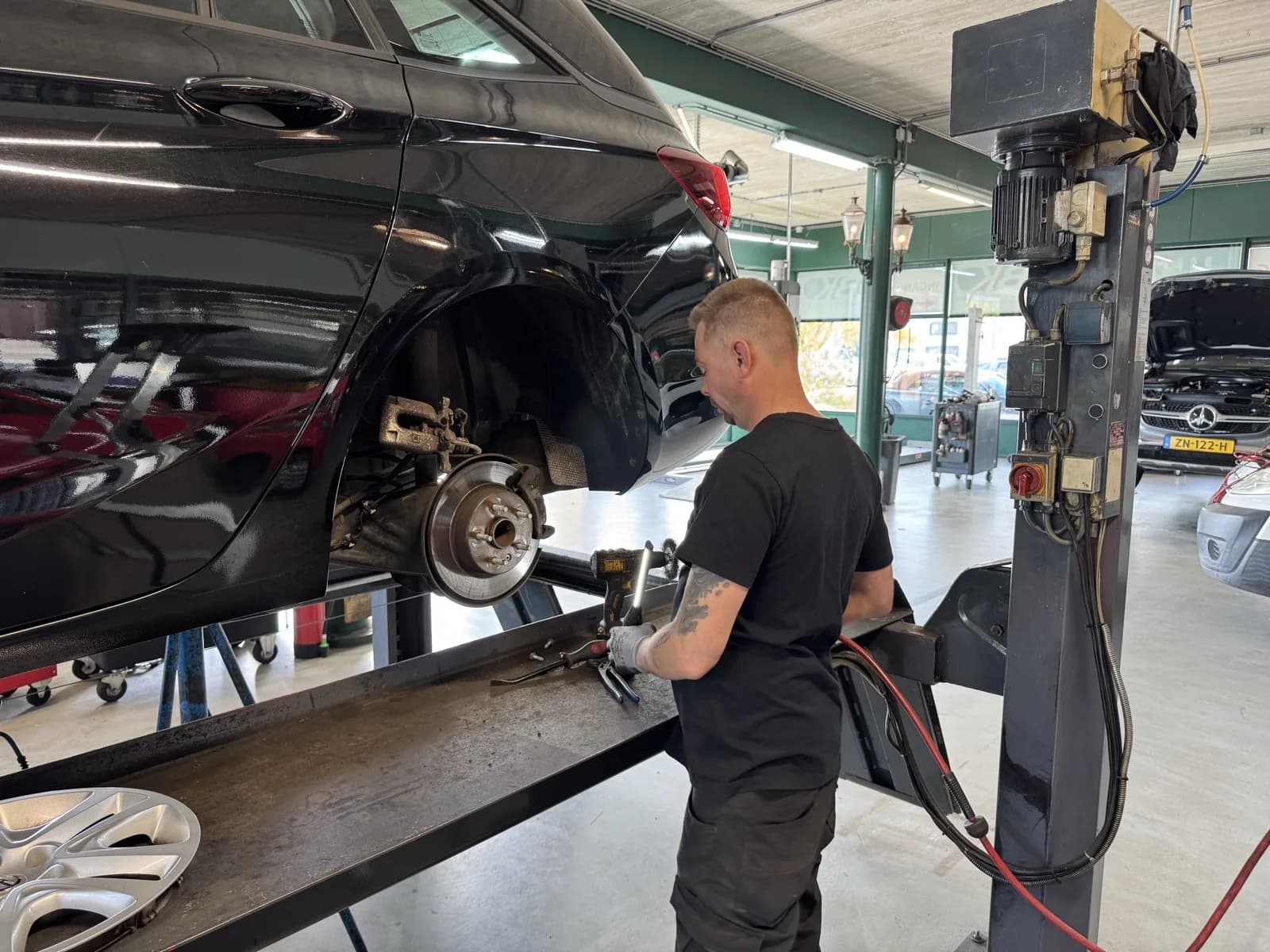 Monteur in MTechniek shirt vervangt remmen op een zwarte Mercedes in de werkplaats Alkmaar