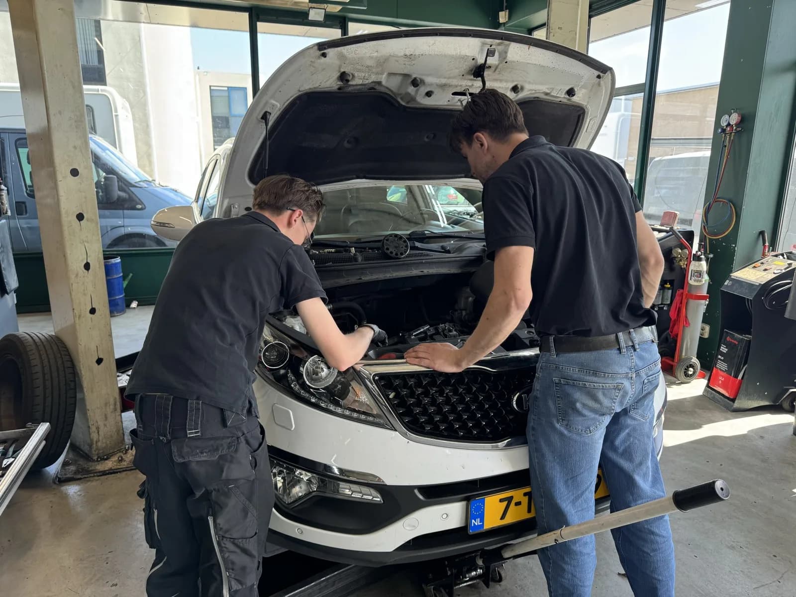 Twee monteurs van MTechniek Alkmaar werken samen aan een KIA in de werkplaats