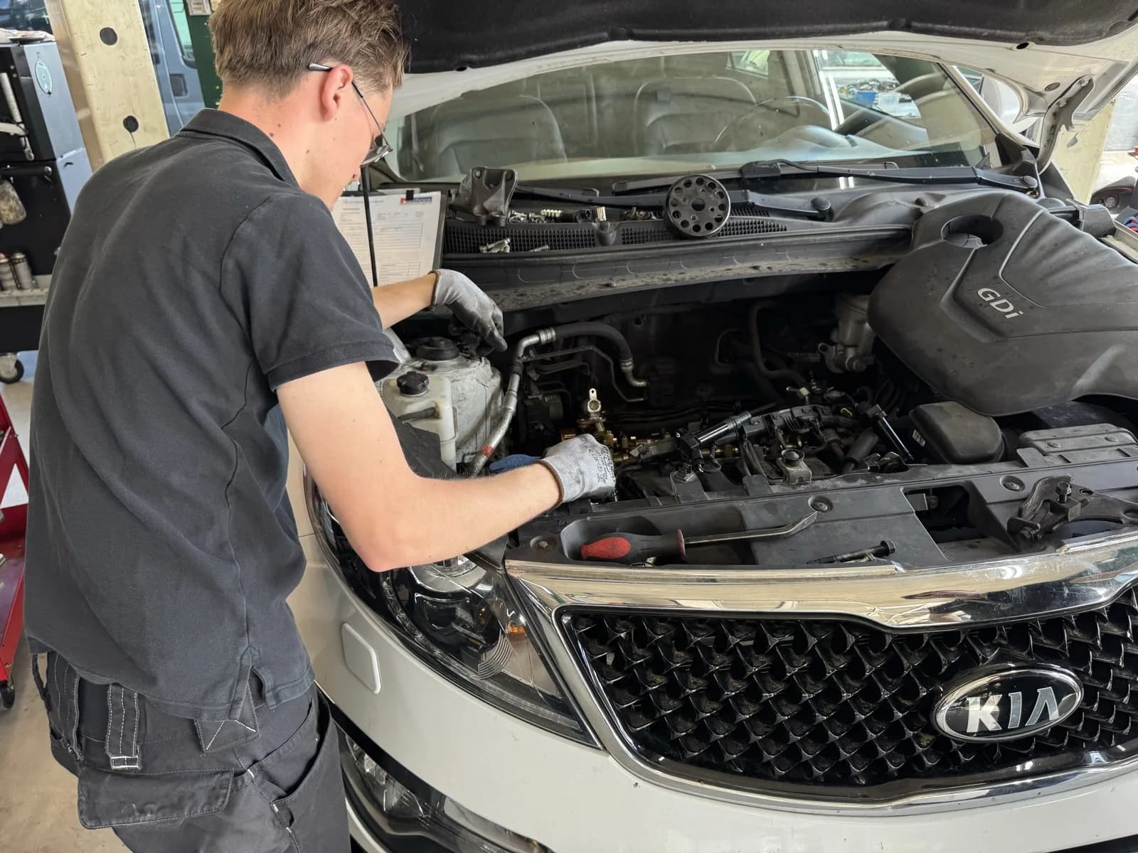 Auto onderhoud, MTechniek Alkmaar vakkundige monteurs Jonge monteur met bril werkt geconcentreerd aan motorblok van auto bij MTechniek Alkmaar